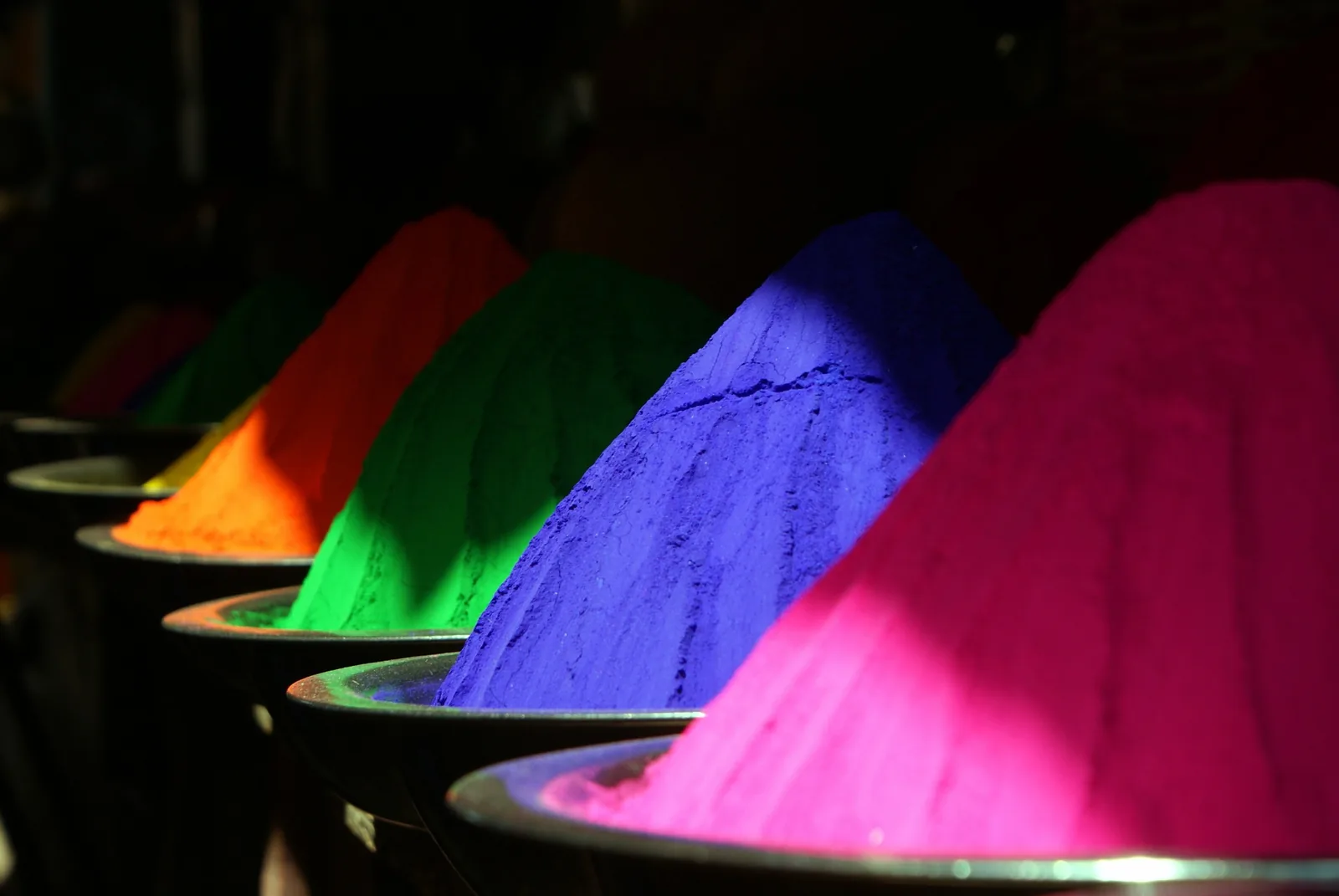 Farbpigmente in Kegeln — Grün, Blau, Magenta, Rot — auf dunklem Grund