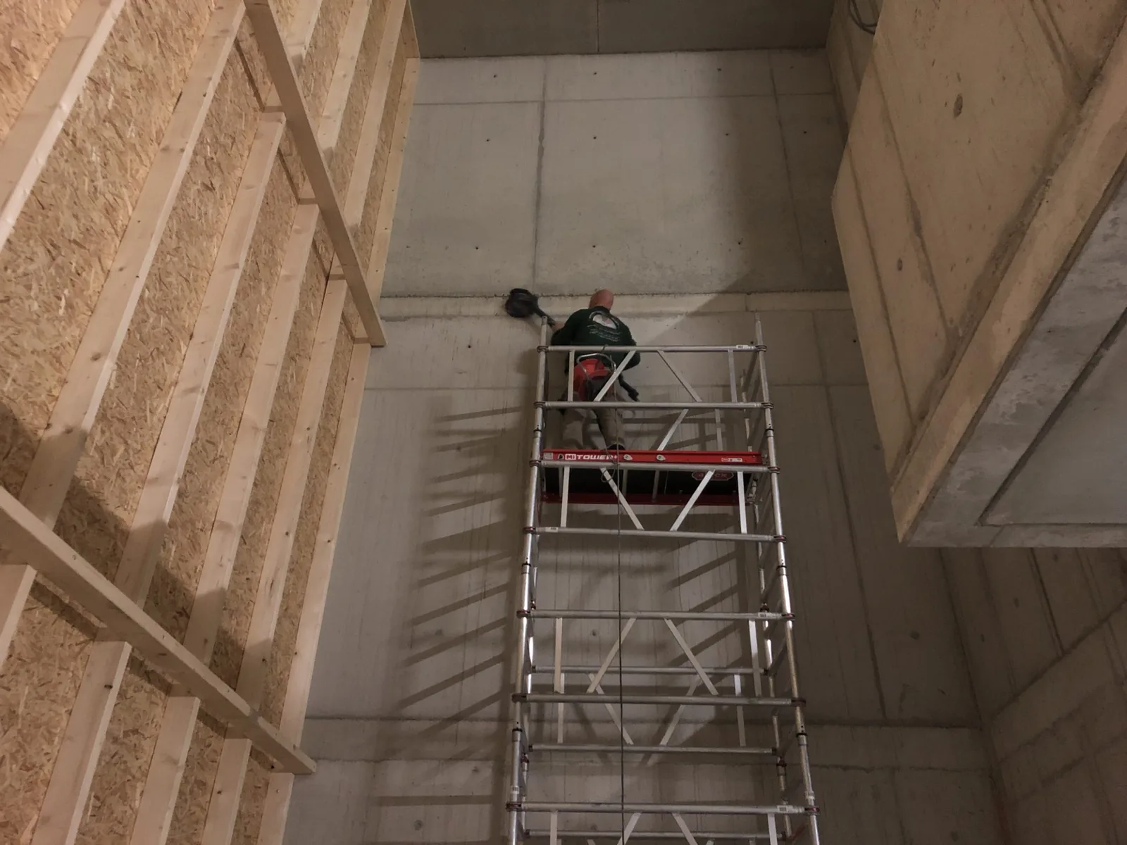 Rollgerüst in einem hohen Treppenhaus, ein Arbeiter oben an der Betonwand