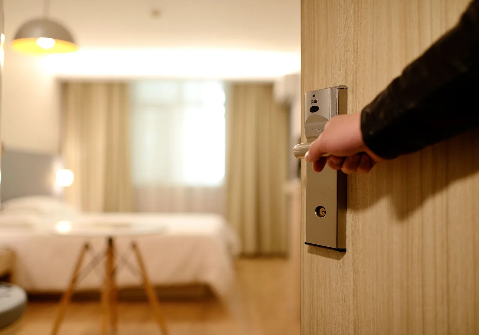 Eine Hand öffnet mit der Karte die Tür zu einem hellen, tadellosen Hotelzimmer